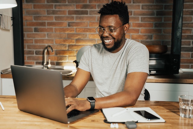 person typing on a laptop while sitting at a kitchen table